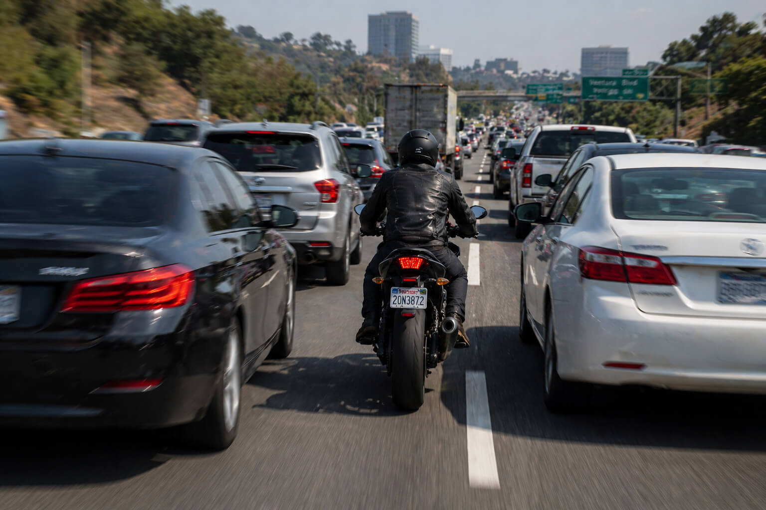 A motorcycle rider lane splitting on a busy multi-lane highway